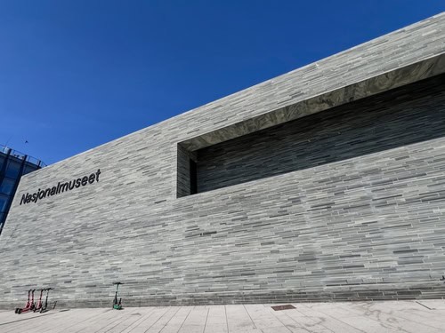 Foto van de gevel van het Nationaal Museum in Oslo met het opschrift "Nasjoinalmuseet", voor het gebouw staan een paar scooters