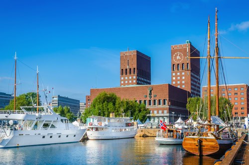 Zicht op de haven van Oslo onder een wolkenloze hemel, op de achtergrond is het stadhuis te zien